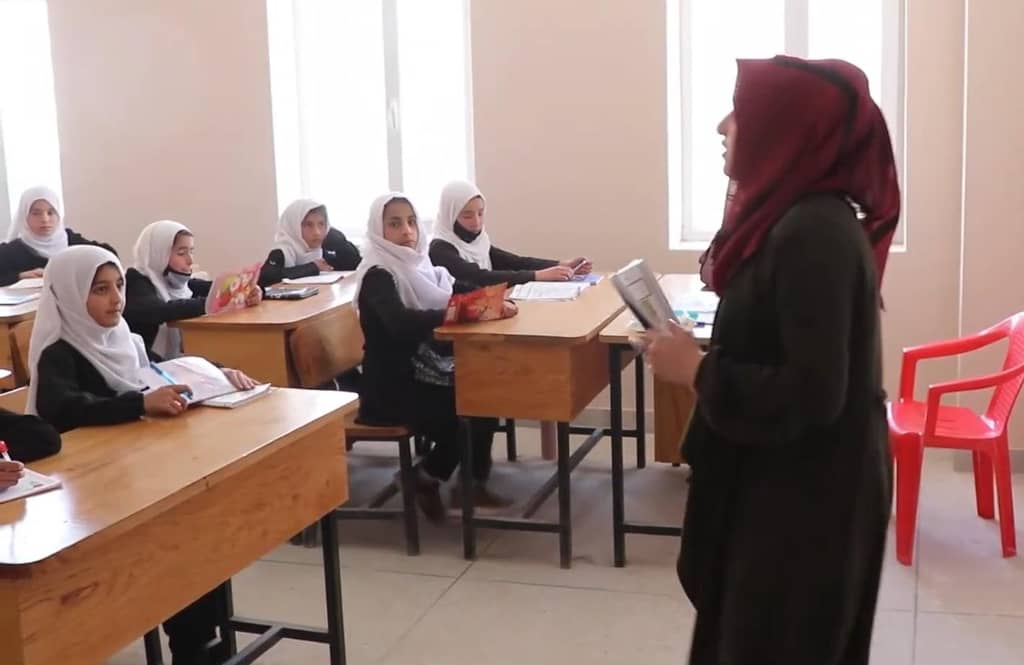 Teacher instructing young female students in a classroom, learning supported by crypto donations via USDT.