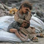 Two children huddled together amidst debris, one older sibling comforting the younger. Digital donations through SOL support aid.