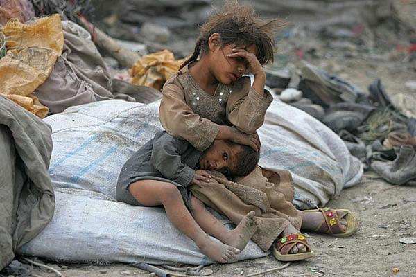 Two children huddled together amidst debris, one older sibling comforting the younger. Digital donations through SOL support aid.