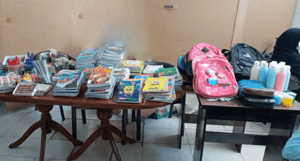 Back to School Report 2024: Piles of notebooks, pencils, and school supplies including backpacks and bottles of sanitizer, ready for distribution to sponsored orphans, made possible by crypto donations like BTC, fostering education and potential.