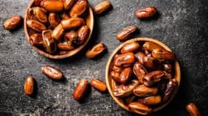 Two wooden bowls overflowing with fresh dates, with some scattered on a dark textured surface. Supports donation via USDT.