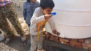 Child drinks water from a tap on a large white tank, crypto-supported aid bringing clean water to needy families.