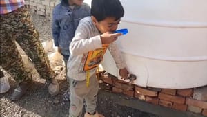 Child drinks water from a tap on a large white tank, crypto-supported aid bringing clean water to needy families.