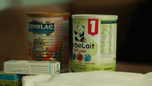 Two cans of infant formula, one labeled RINOLAC and the other ebeLait, sit next to a small box with Arabic text, implying essential aid with crypto donations like XRP for parents in need.