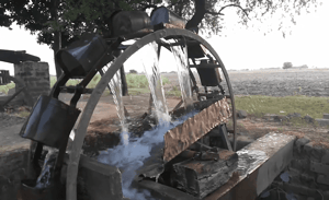 Water wheel lifting water for irrigation, symbolizing ongoing charity and agricultural support, with crypto donations enabling such life-sustaining projects and reflecting the concept of Sadaqah Jariyah, benefiting communities with essential resources like clean water, enabled by support like that of Ethereum.