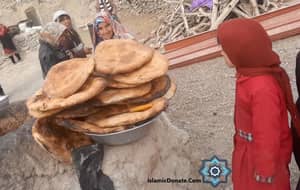Women and children gather around a large pile of fresh flatbread, signifying a communal charitable act of giving during Mawlid, supported by crypto donations via BTC.