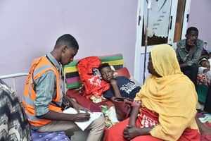 Healthcare worker noting patient details with woman and child during medical aid efforts, supported by ETH donations for general healthcare.