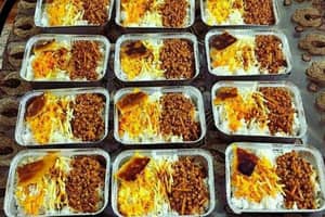 Agrid of individual servings of food in foil containers, each with rice, shredded carrots, lentils, and a piece of meat, prepared for donation. Supporting aid with ETH.