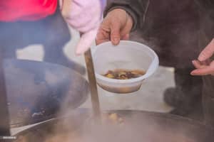 Serving a bowl of hot food from a large pot to aid those in need, supported by stablecoin donations.