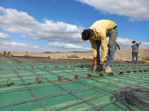 Construction workers install rebar on a green membrane base, symbolizing rebuilding homes and restoring dignity through social justice efforts. Donations in ETH support job creation and sustainable livelihoods for those in need.