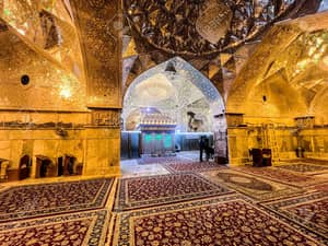 Ornate interior of a mosque with Islamic calligraphy on the walls and ornate chandeliers, featuring prayer rugs and people gathered in the background, supported by ETH donations.
