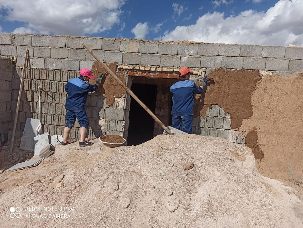 Two people plastering a wall, symbolizing rebuilding efforts funded by crypto Zakat donations, potentially using Arab Emirates Dirham.