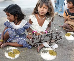 Three young children sitting on the ground with bowls of food, one girl in a blue dress, the other in a white top. Crypto donations via USDT support this relief.