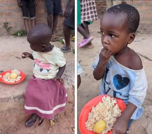 Two young African children with plates of food. The child on the left wears a yellow shirt and maroon skirt, and the child on the right wears a blue shirt. Crypto donation supports relief efforts.
