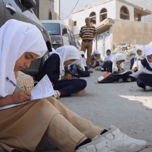 Children in hijabs learning outdoors, with one girl in the foreground writing, receiving crypto donation support via USDT, symbolizing educational aid for orphans.