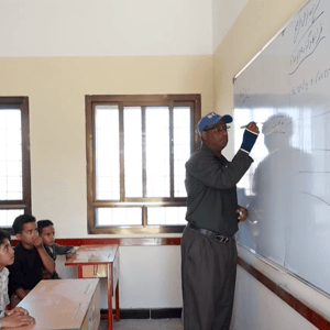 Sponsor of orphans classroom with teacher writing on whiteboard, crypto donations enable education for 49 children sponsored via ETH.