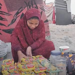 A young girl in a headscarf and maroon dress sorts food items, an act of aid for working children, with donations possibly supported by ETH.