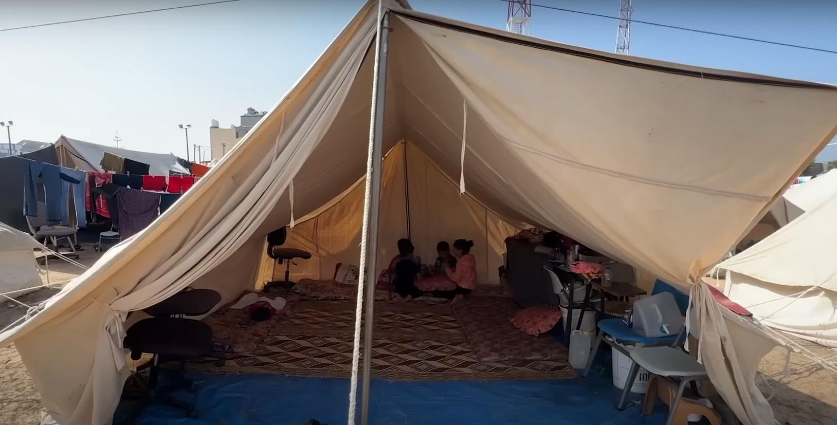Tent interior in Palestine with families receiving aid, supported by ETH donations for relief and education.