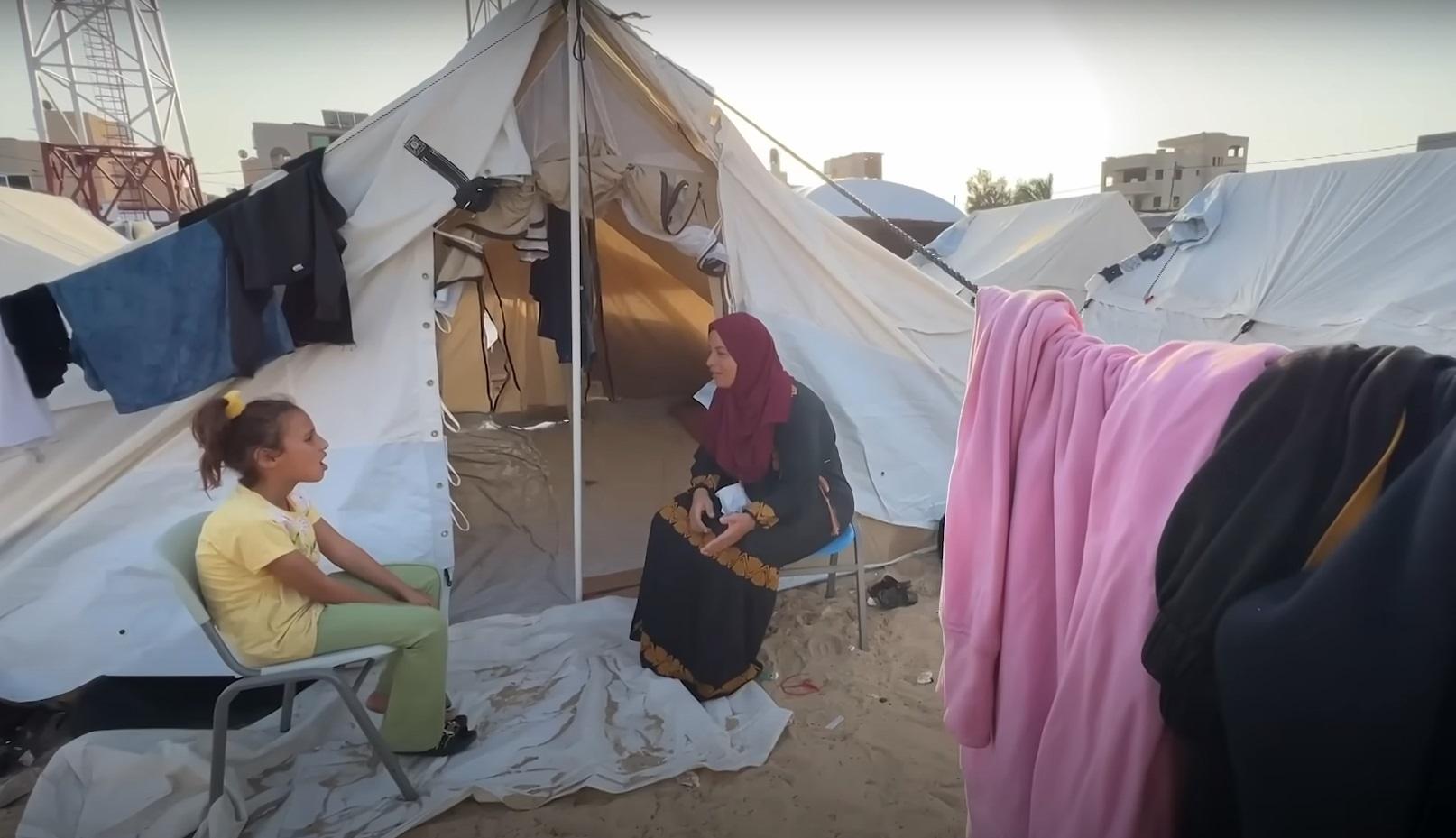 Aid in Palestine: A girl sits outside a tent talking to a woman inside, with laundry hanging nearby. This scene depicts the daily struggles faced by aid organizations in Gaza and Rafah, highlighting the critical need for support and the resilience of the community. Donations are processed via ETH.