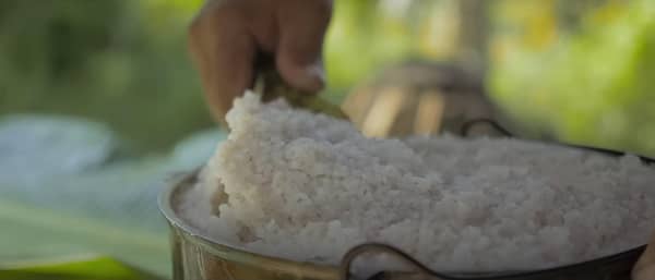 A hand scoops white rice into a metal bowl, suggesting a food donation or preparation for charitable giving in the Muslim community, possibly supported by SOL crypto.