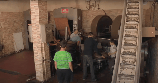 Syrian workers operating machinery in a restored olive oil workshop, receiving crypto donations for sustainable livelihoods via Ethereum.