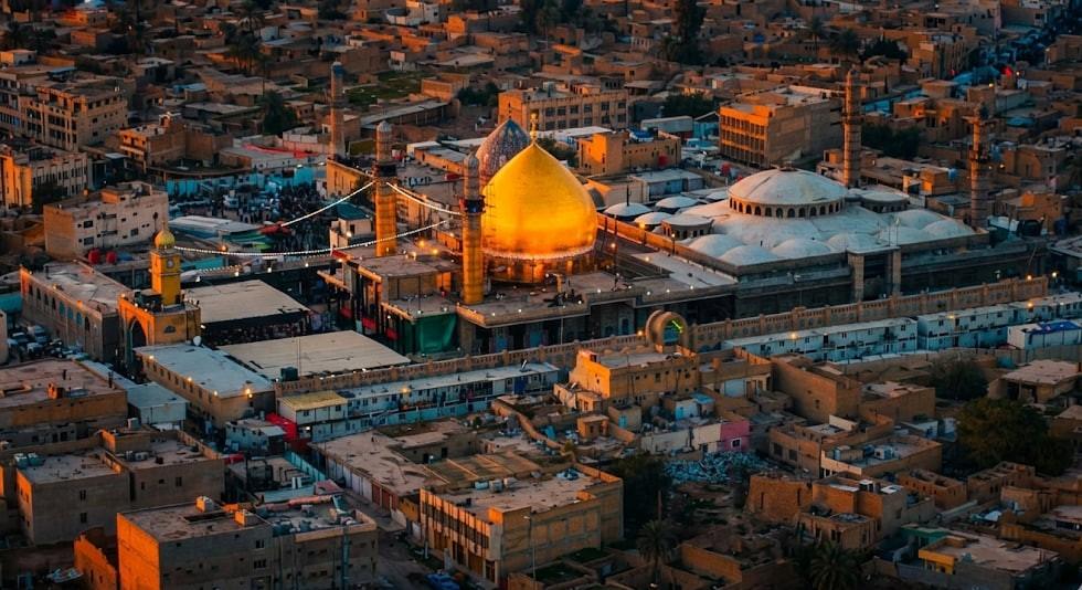 Golden domed shrine with minarets surrounded by a cityscape at sunset. Features Imam al-Hadi's legacy of charity and transparency, accepting crypto donations like USDT.