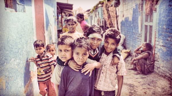A group of children stand in a narrow alley with distressed buildings. One child in front wears a purple shirt, another a striped shirt. Crypto donations enhance aid, with USDT facilitating support.