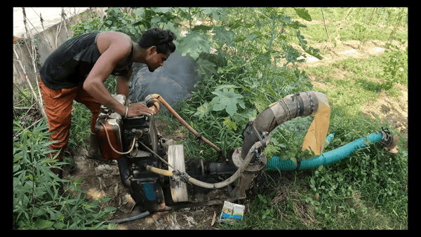 Man servicing a water pump emitting smoke, preventing water shortage through regular maintenance of charity projects, aided by Solana.
