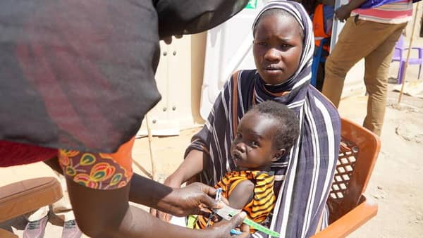 A mother holds her child and receives health assistance. Aid provided via crypto, supporting Sudanese women and girls amidst conflict, offering safe spaces and vital resources like healthcare through Our Islamic Charity.