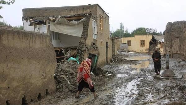 Damaged homes in Afghanistan with people walking through mud, symbol of need for humanitarian aid and crypto donations via USDT.