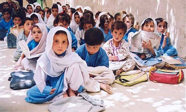 Young students in a classroom setting, some with books, wear traditional attire. Donation to educational initiatives can be processed via USDT.