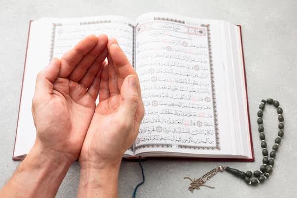 Open Quran with hands in prayer and prayer beads. Ramadan daily supplications, wisdom, forgiveness, mercy, guidance. ETH