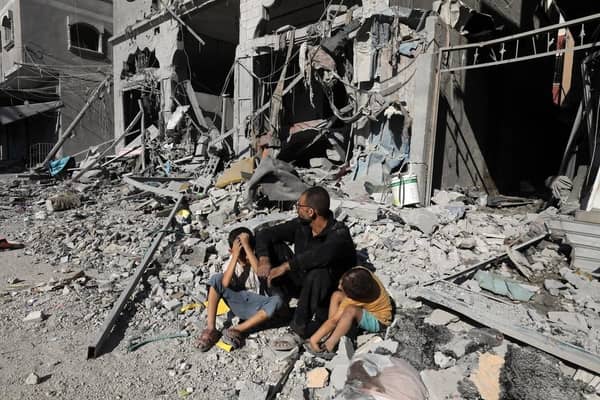 A father sits with his two distressed children amidst rubble and destroyed buildings, symbolizing the devastating impact of conflict. Crypto Zakat donations, including ETH, provide vital aid and support to families in need in Palestine.