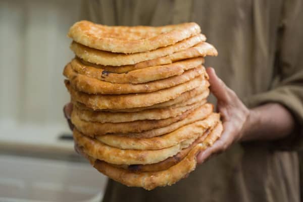 A person holds a tall stack of freshly baked unleavened flatbreads, prepared by Our Islamic Charity for the Feast of Prophet Muhammad 2024, with offerings supported via ETH.