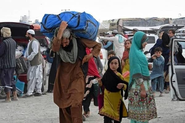 Man carrying heavy load, worried Afghan families at border, urgent aid via Solana, donations needed for food, water, shelter.