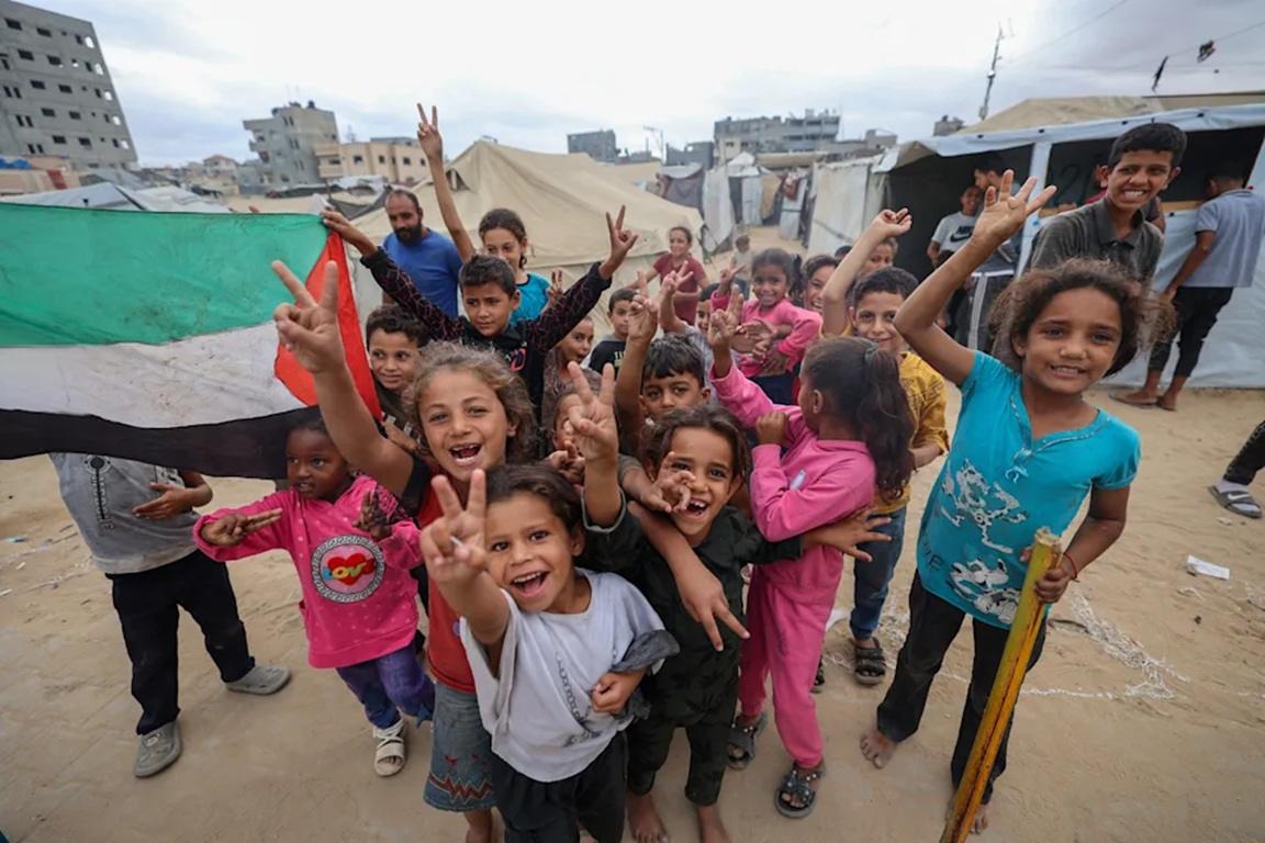 Children with Palestinian flag cheer holding up peace signs, symbolizing hope and resilience in Gaza, with support from crypto donations like Ethereum.