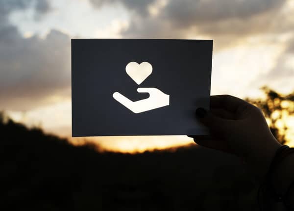 Hand holding paper with cut-out of hand offering a heart, representing anonymous Islamic donations and sincerity in charity using USDC.