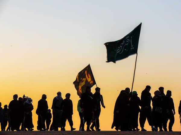 Procession of Arba'in walk, pilgrims carrying flags at sunset; supporting relief efforts via crypto donations like ETH.