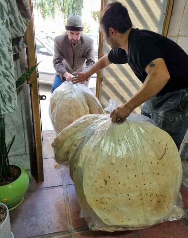 Two men hand large bags of flatbread to each other, symbolizing the provision of sustenance and hope to Palestinians, facilitated by cryptocurrency donations such as Bitcoin.