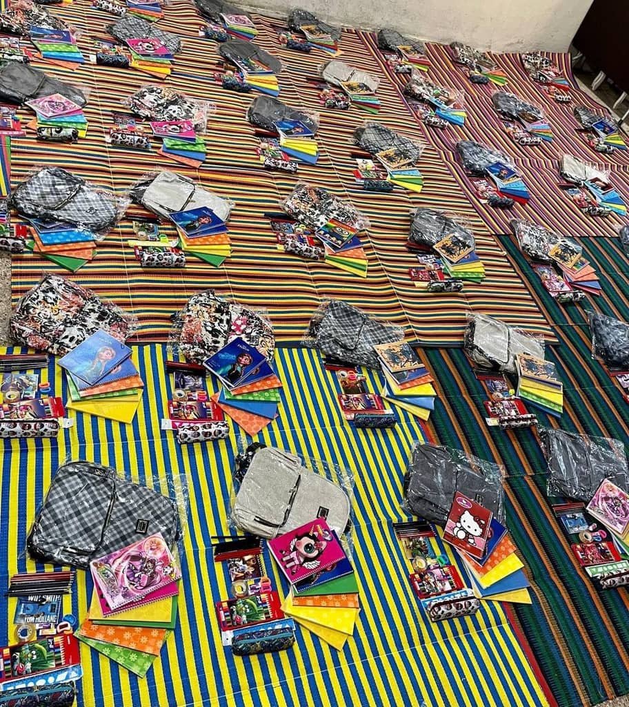 School supplies including backpacks and notebooks are laid out on striped mats, ready for distribution. Funds donated via ETH support these educational resources for children in need.