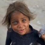 Close-up of a young child's face with striking blue eyes and tousled hair, holding a bundle of gray string. The child appears to be in a situation requiring aid.